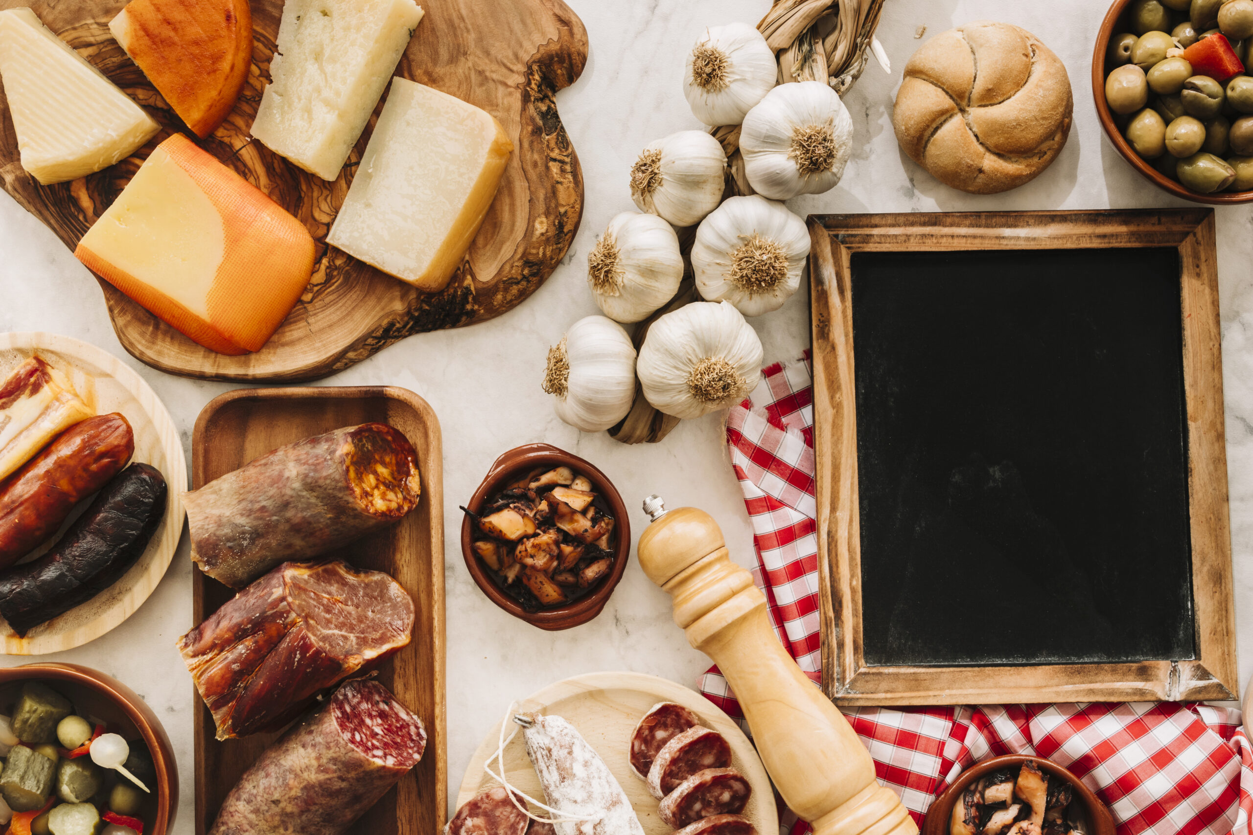 Composizione di prodotti tipici con formaggi, salumi, olive, aglio e lavagna su tavolo rustico