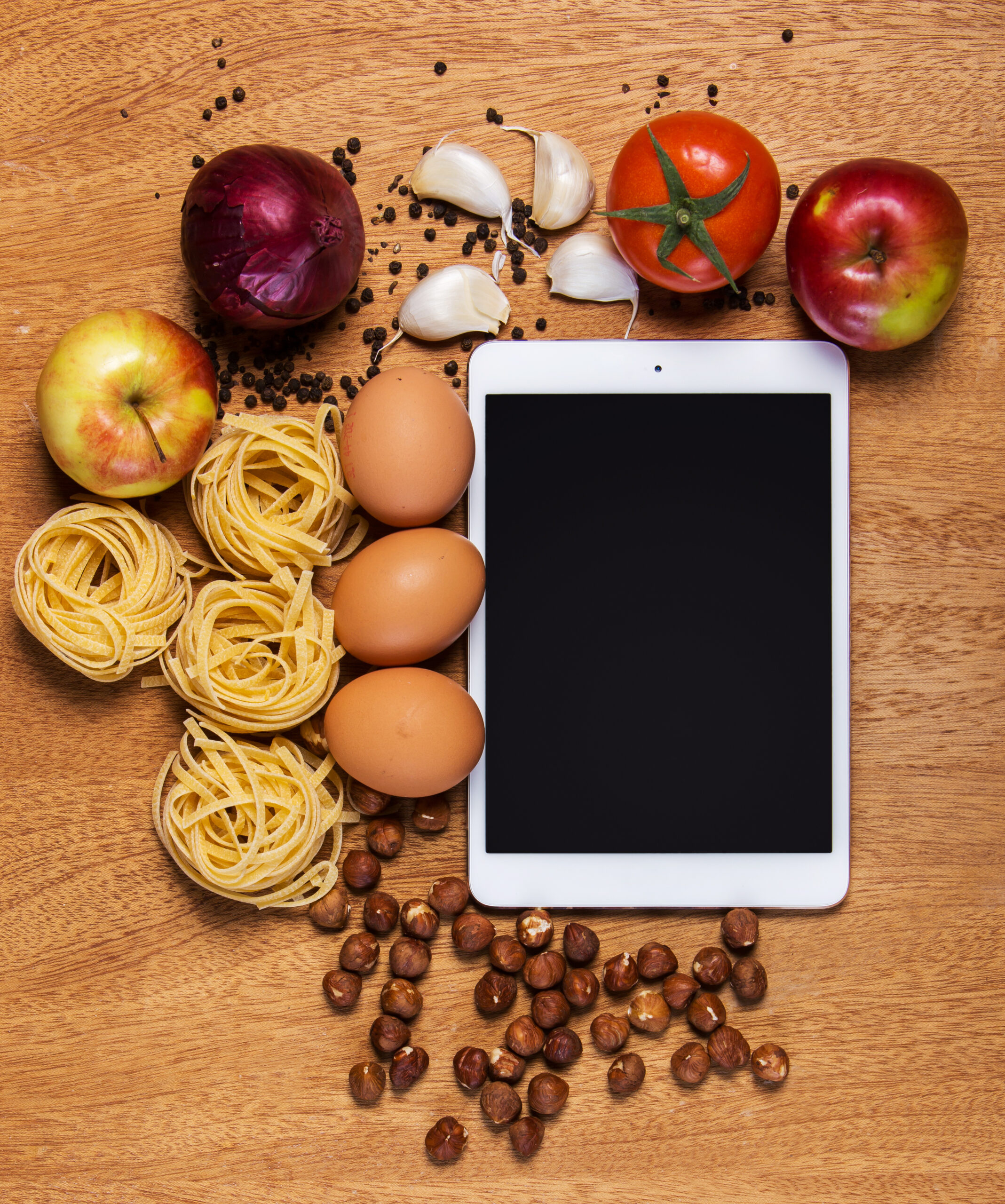 Tablet con ingredienti da cucina e prodotti alimentari disposti su tavolo in legno