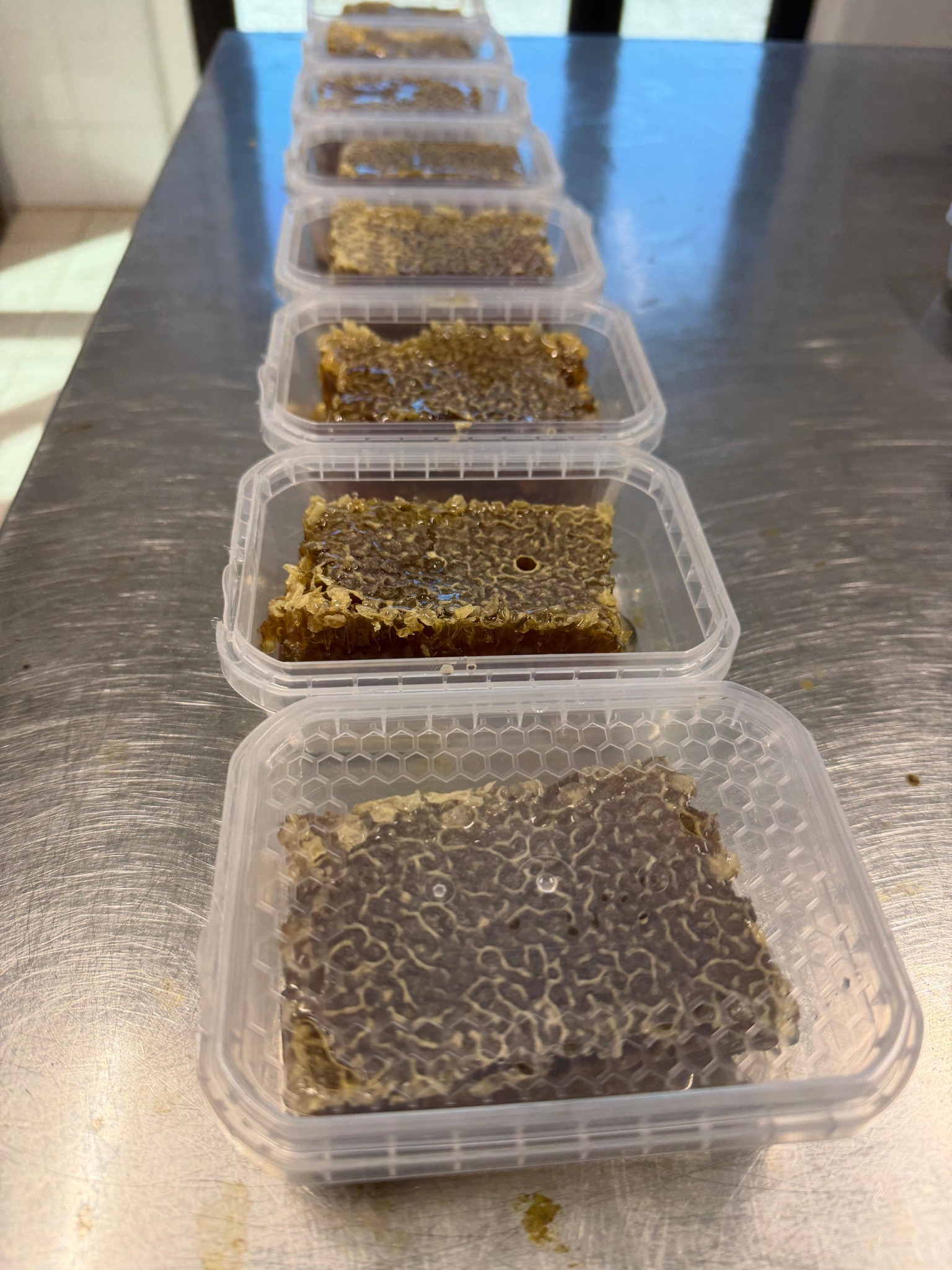 Confezioni di miele in favo artigianale disposte in fila su banco da laboratorio
